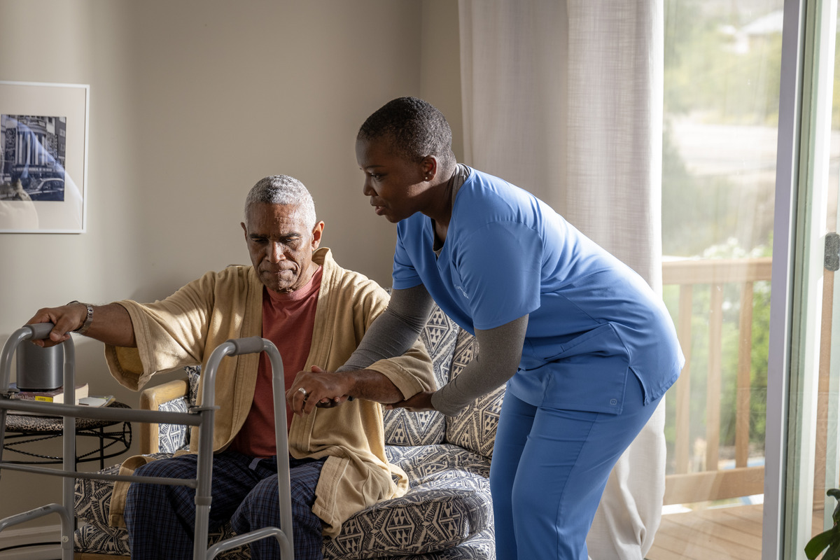 A caregiver helping an older man stand from a chair at home